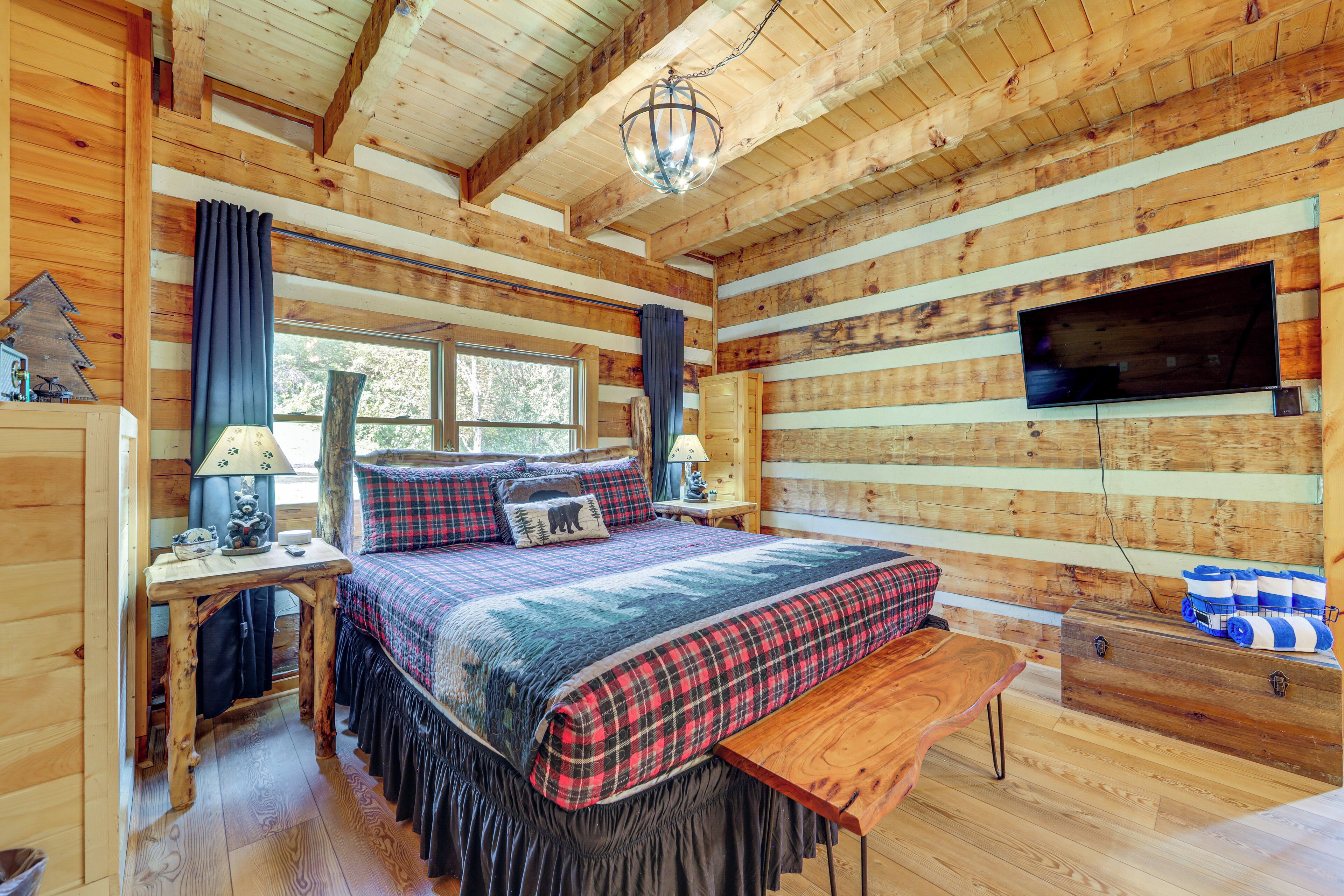 A cozy log cabin bedroom with a large bed, a wooden desk, a dresser, and a television mounted on the wall.