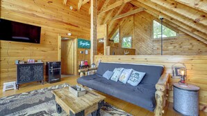 Interior acogedor de una cabaña de madera con sofá, televisor de pantalla plana, mesa de centro de madera y una lámpara rústica.