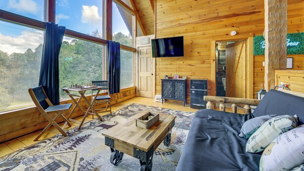 Una cabaña acogedora con un ventanal grande, paredes de madera, un televisor de pantalla plana, una mesa de comedor y un sofá.