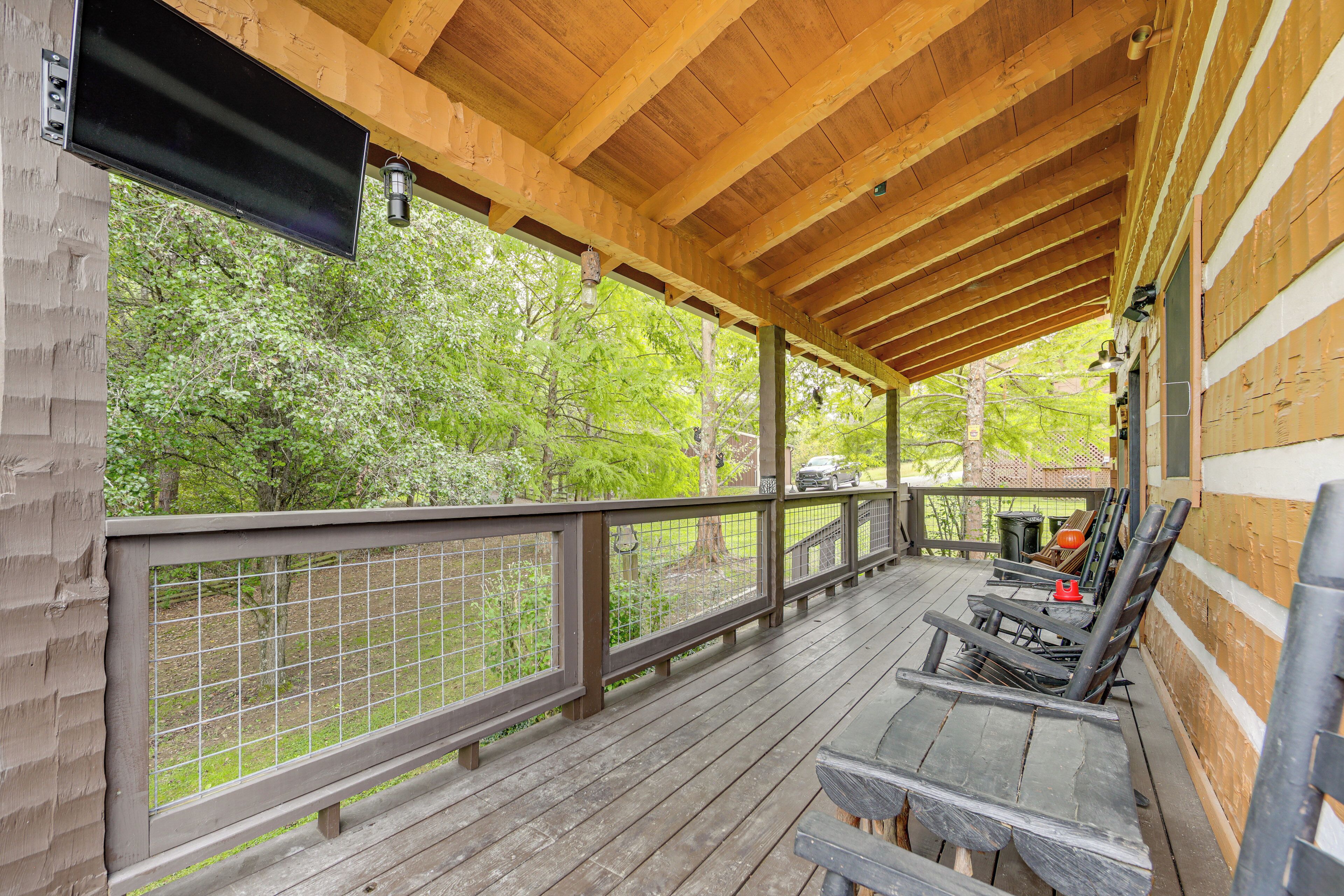 Une terrasse en bois couverte, dotée de sièges extérieurs et offrant une vue sur les arbres.