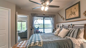 A bedroom with a large bed, a ceiling fan, a window with curtains, and a view of a balcony. - Table Rock Lake Retreat: Steps to Water & Pools! (Kimberling City)