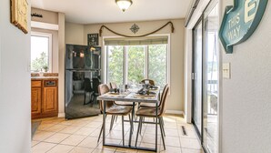 A kitchen with a dining table, chairs, a refrigerator, and a window with blinds. - Table Rock Lake Retreat: Steps to Water & Pools! (Kimberling City)