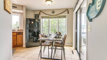Una cocina con una mesa de comedor para cuatro personas, un refrigerador y una ventana con vista a árboles.