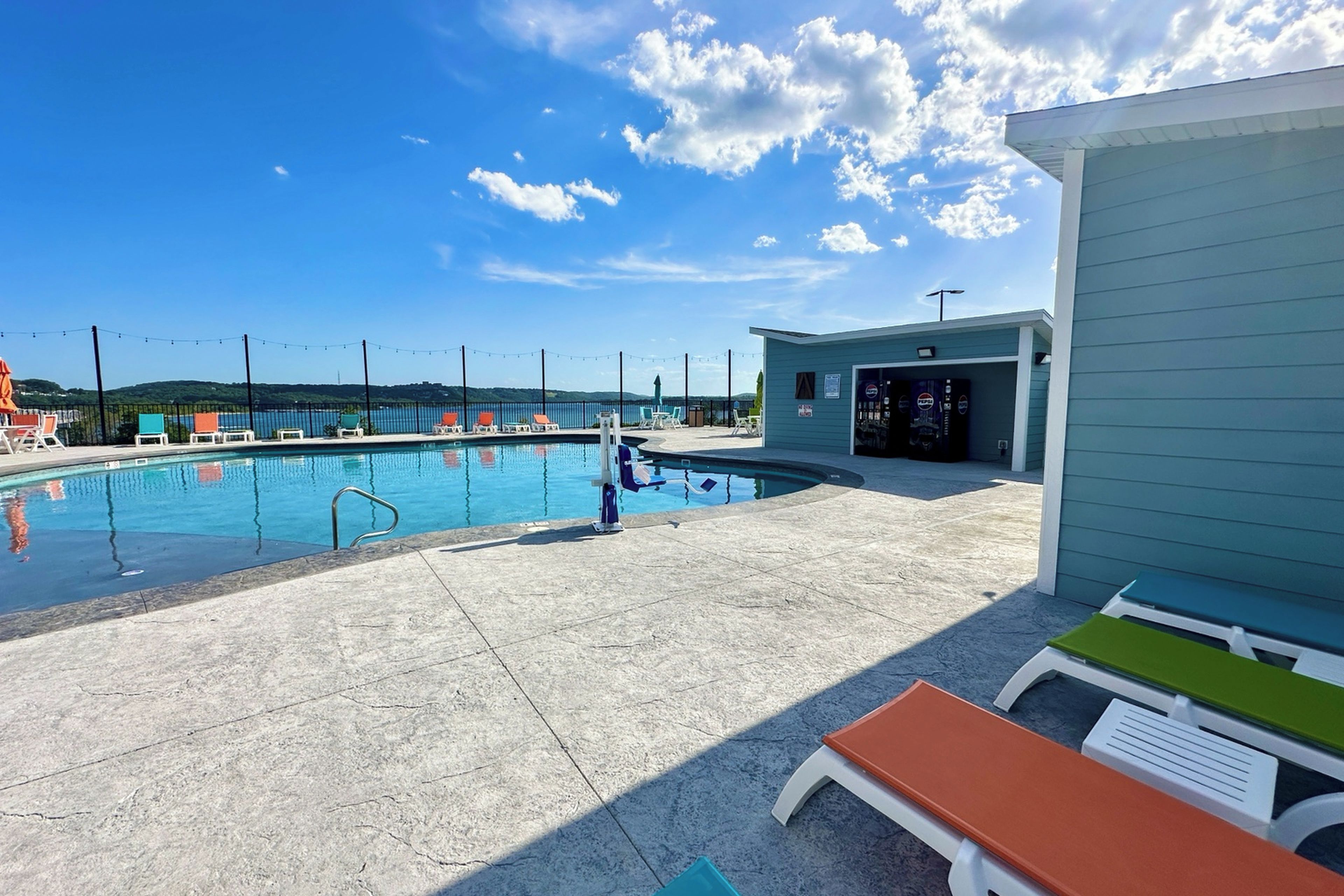 A swimming pool with lounge chairs and a small building, likely a snack bar, in the background.