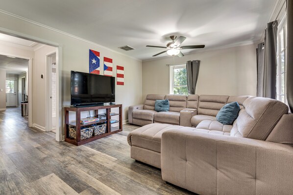 A living room with a sectional sofa, a TV on a wooden stand, and a ceiling fan. - Steps to Playground: Family Home in Douglasville! (Douglasville)