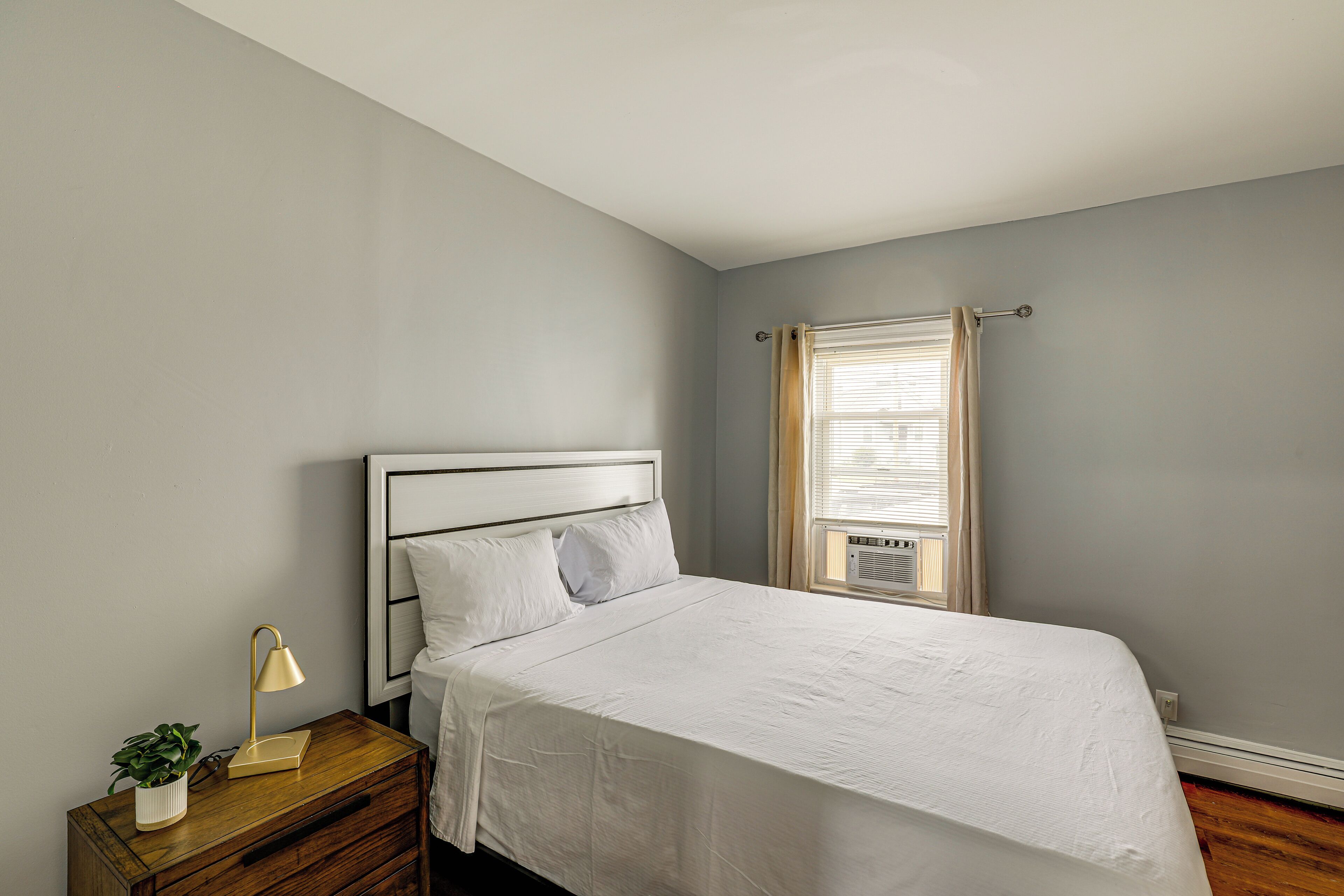 A bedroom with a bed, a nightstand, a lamp, and a window with curtains.