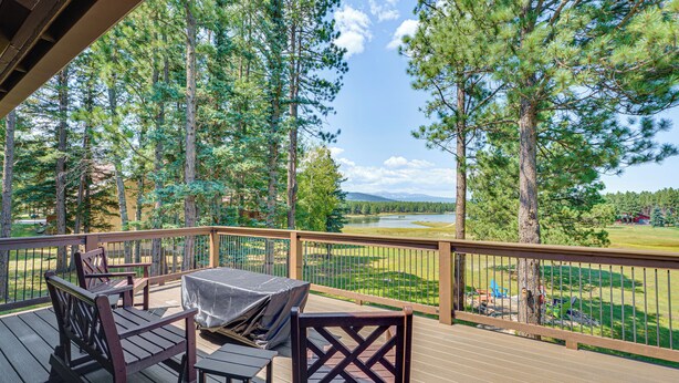 Terraza de madera con mobiliario exterior, con vista a un lago y zona boscosa.