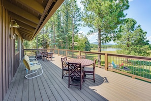 A wooden deck with a table and chairs, overlooking a lake and forest.