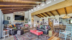 Un amplio salón con chimenea de piedra, mobiliario de cuero y un televisor grande.