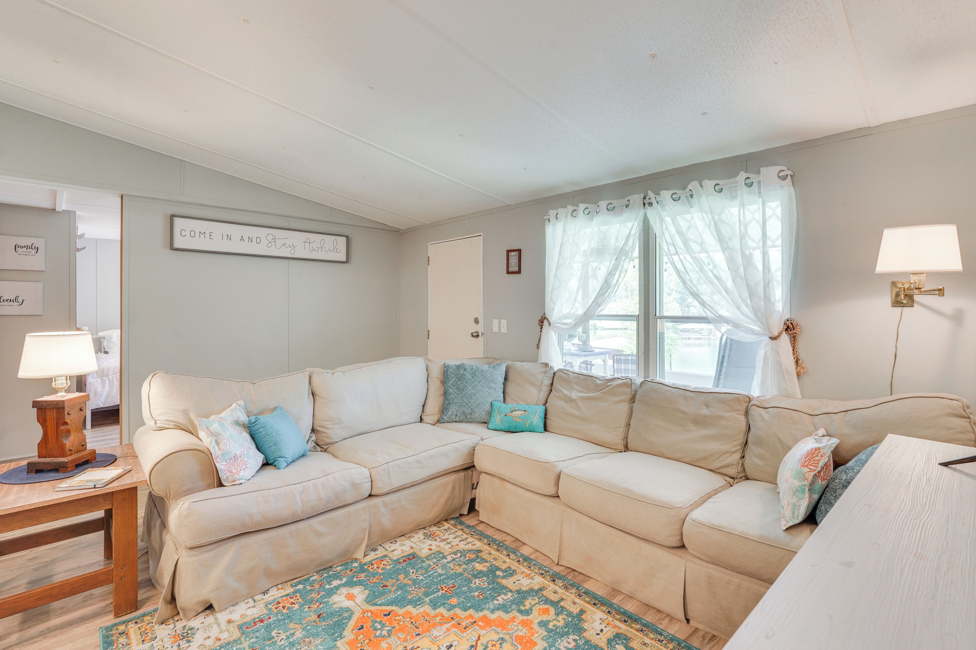 A cozy living room with a sectional sofa, a wooden side table, a patterned rug, and a window with sheer curtains.