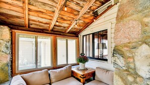 A cozy seating area with a stone wall and wooden ceiling, featuring a cushioned bench and a small table with a potted plant. - Houghton Lake Cabin: 0.3 Mi to Beach & Pier! (Prudenville)