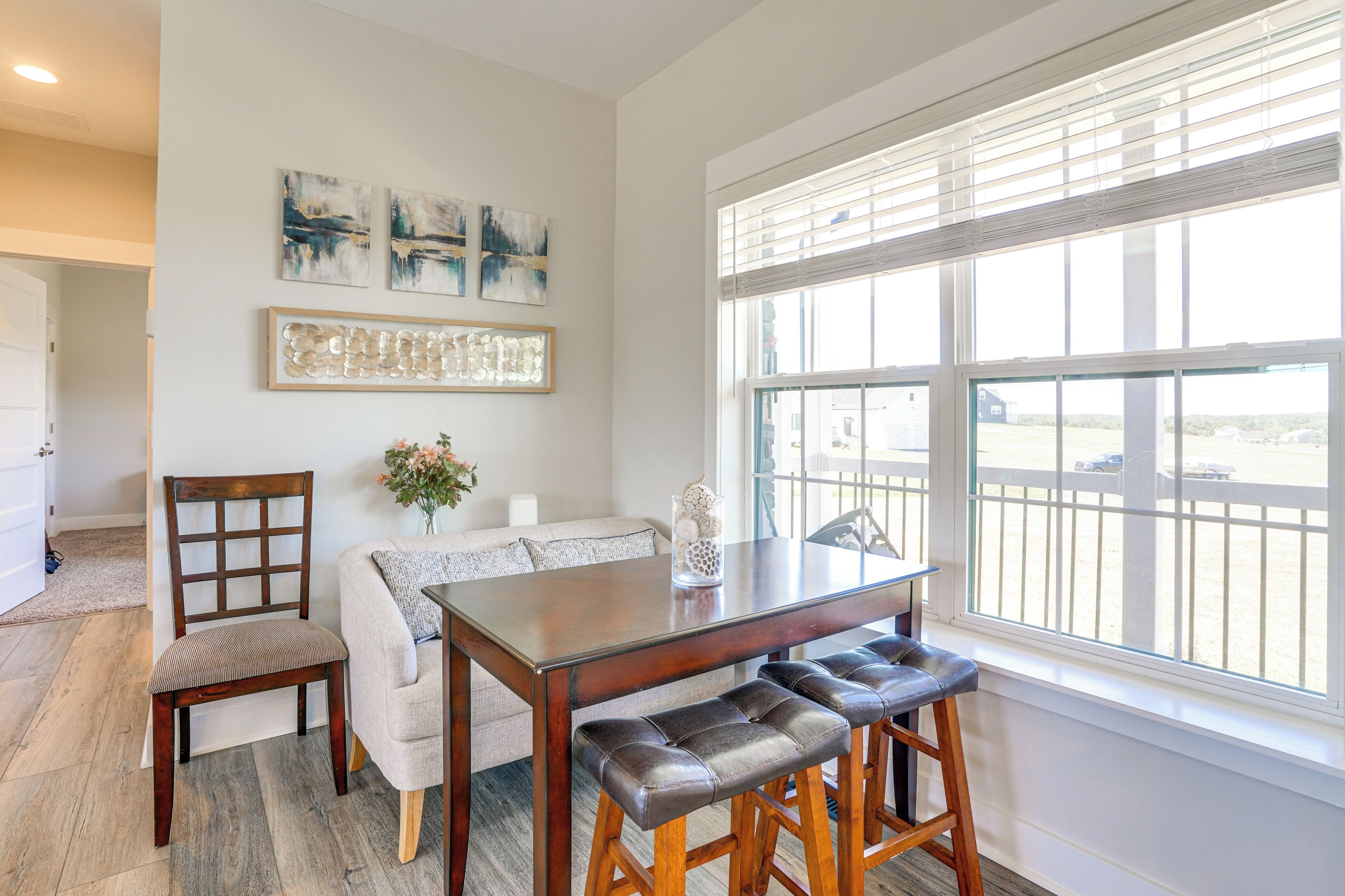 A dining area with a wooden table and leather barstools, a cushioned bench, and a vase with flowers.