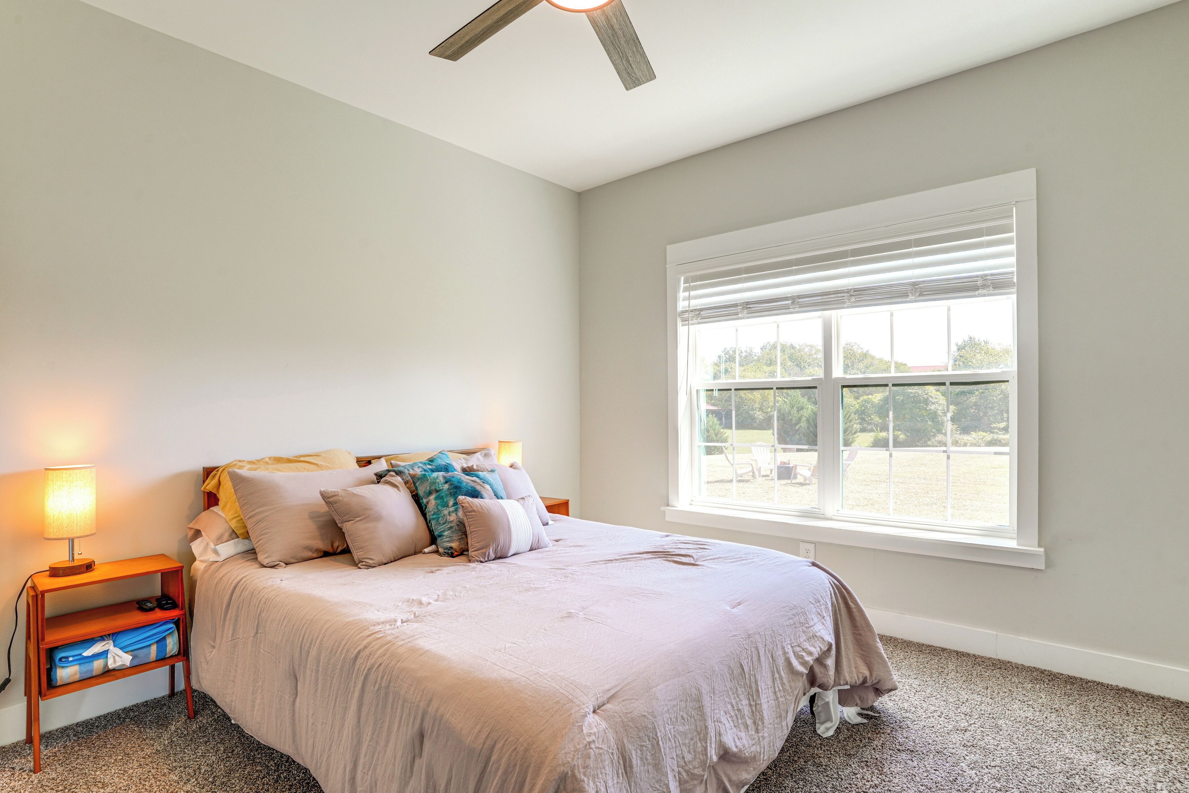 A bedroom with a bed, a nightstand, a lamp, a window with blinds, and a ceiling fan.