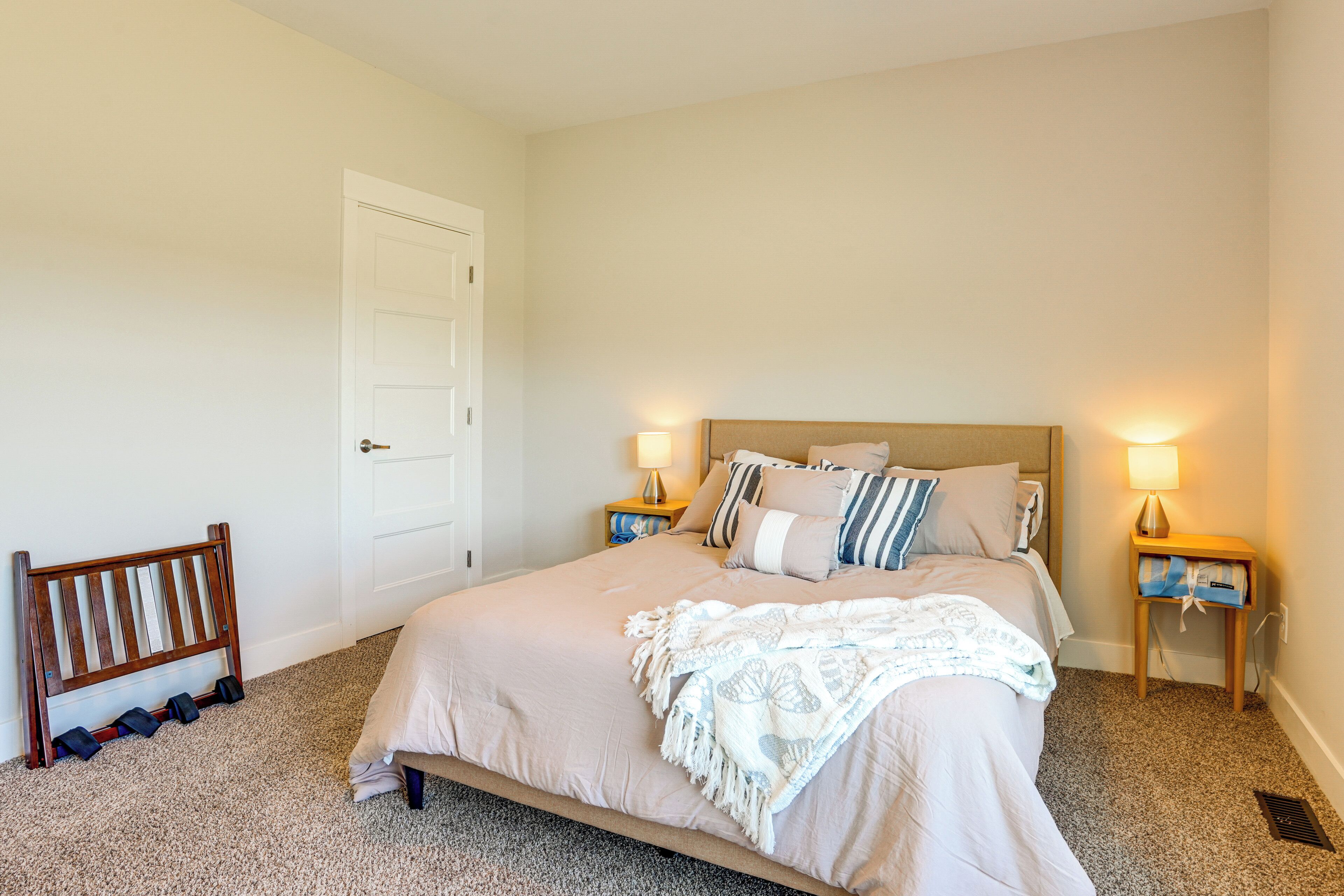 A bedroom with a large bed, two bedside tables with lamps, a wooden bench, and a door.