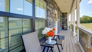 Un espacio al aire libre techado, con pared de piedra, ventanas amplias y una mesa con sillas.