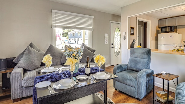 A modern living room with a dining table set for four, a grey sofa, a blue armchair, and a kitchen area visible through an open door. - 3 Mi to Dtwn & Flood Museum: 'cozy Q Cottage' (Johnstown)