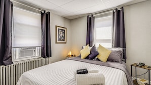 A neatly made bed with striped bedding, a bedside table with a lamp, and a framed picture on the wall. - 3 Mi to Dtwn & Flood Museum: 'cozy Q Cottage' (Johnstown)