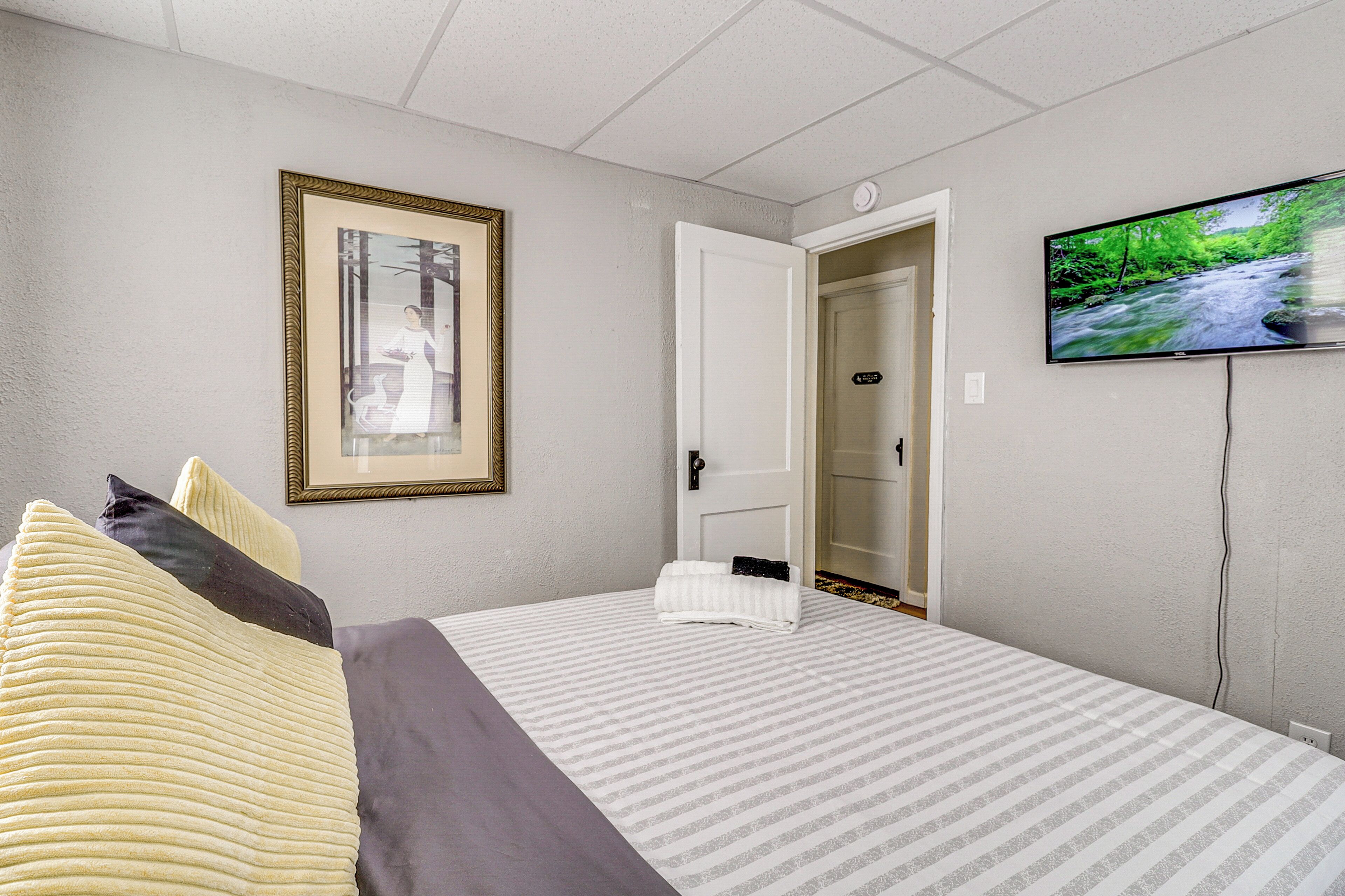 A hotel room with a bed, a framed picture on the wall, a television, and a door leading to another room.