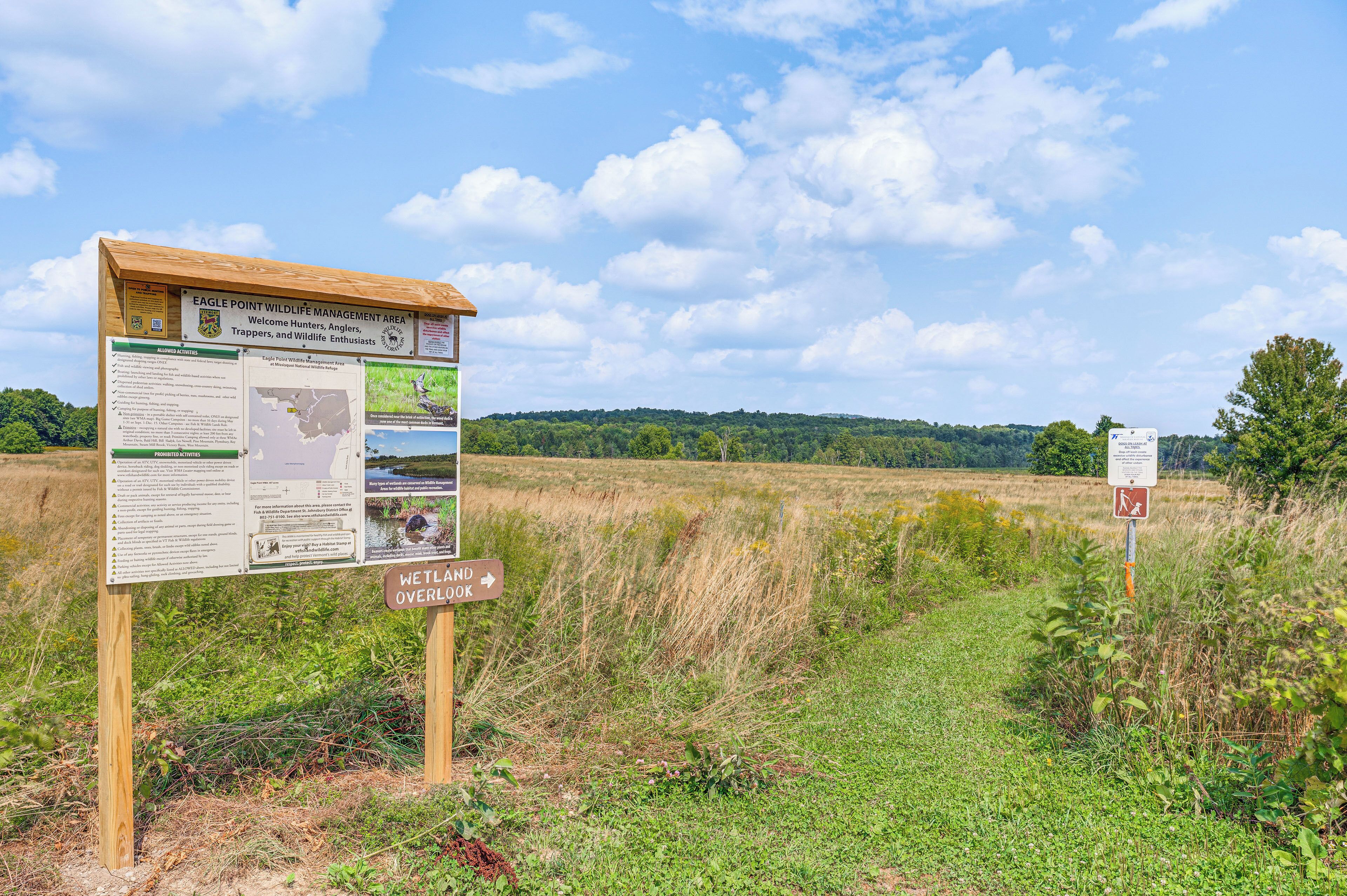 Un panneau indiquant une zone de gestion de la faune, avec des informations sur les activités autorisées et interdites, une carte et un panneau de signalisation indiquant la direction d’un point de vue sur une zone humide.