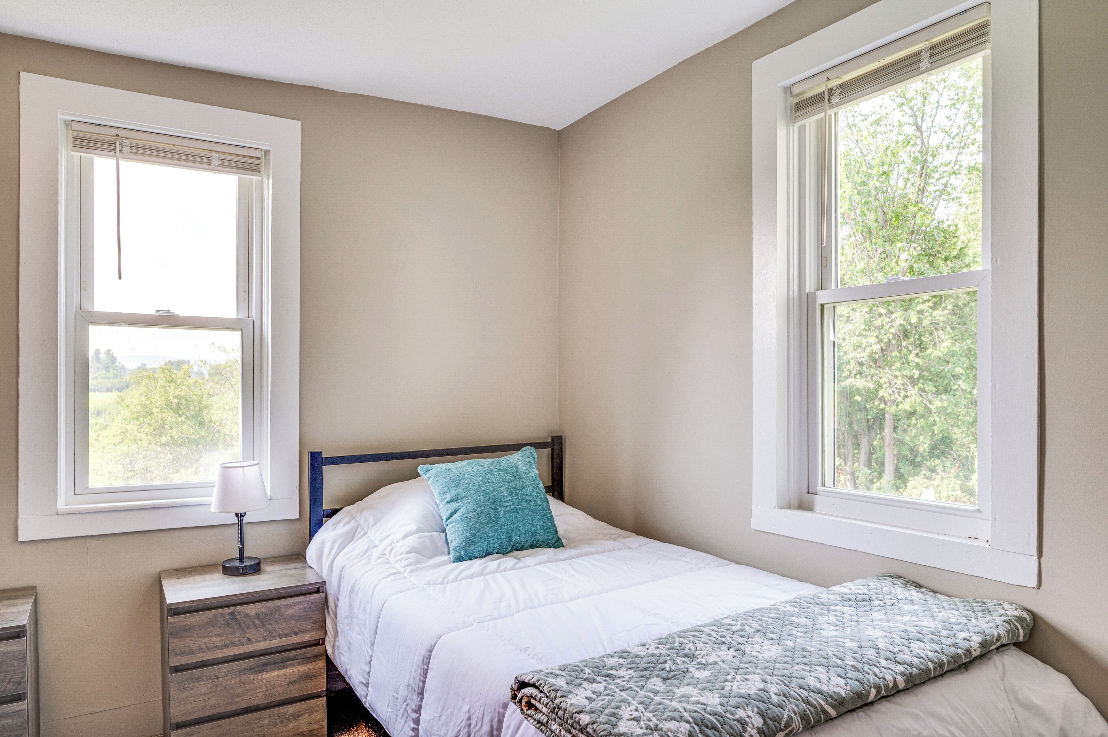 A bedroom with a bed, a nightstand, a lamp, and two windows.