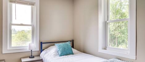 A bedroom with a bed, a nightstand, a lamp, and two windows.