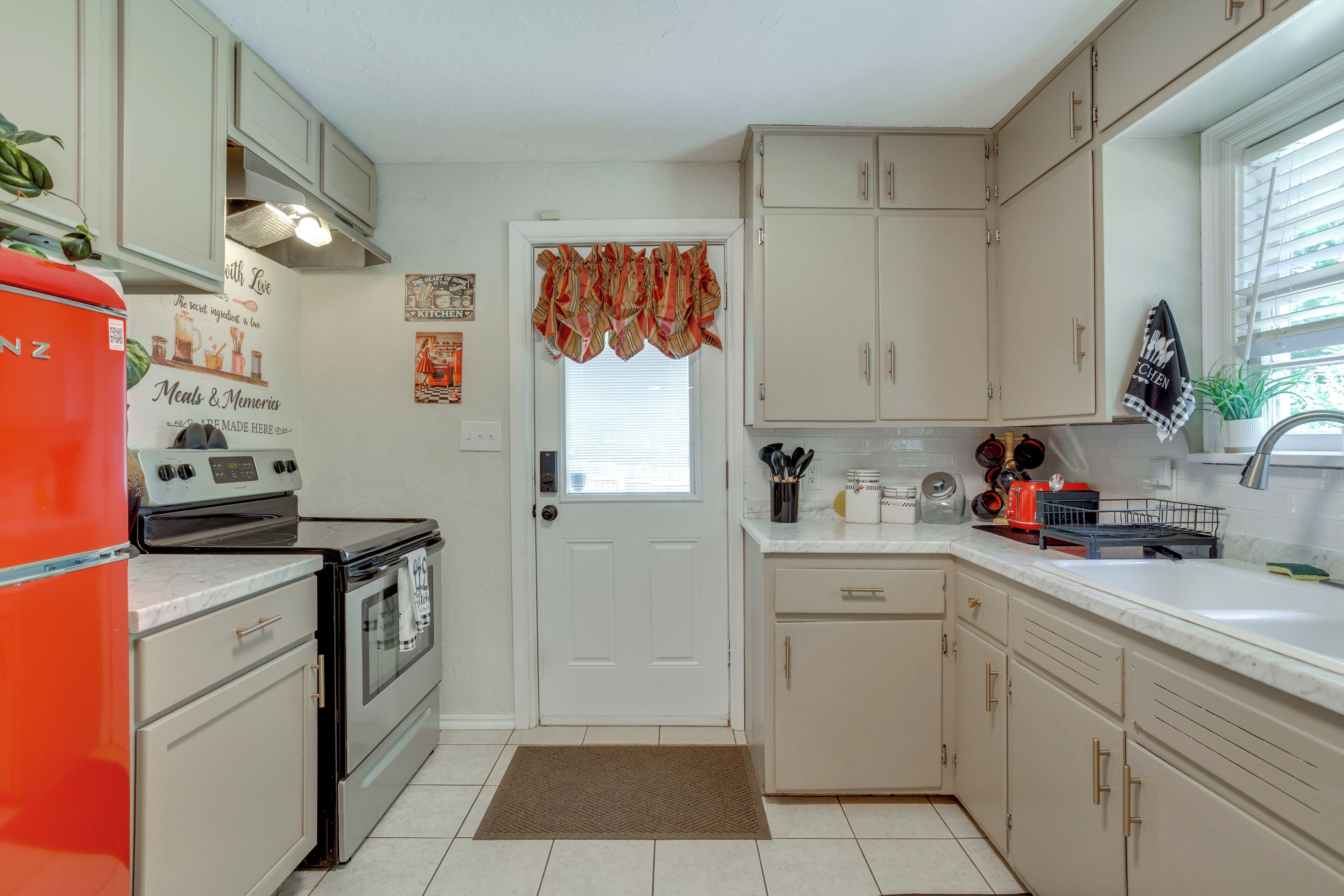 A kitchen with white cabinets, a red refrigerator, a stove, and a window with curtains.