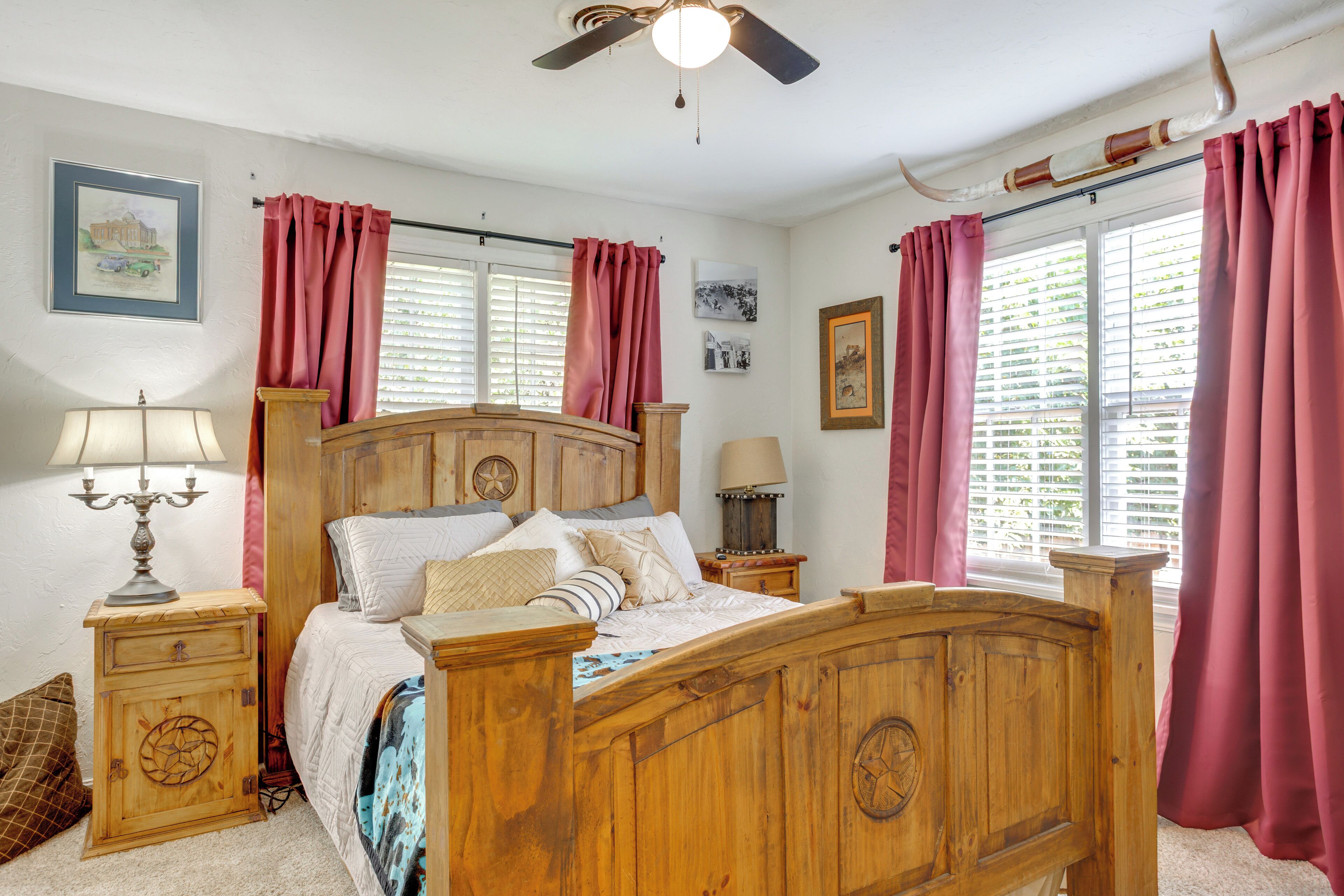 Un dormitorio con una cama de madera, dos mesitas de noche, un ventilador de techo y una ventana con cortinas.