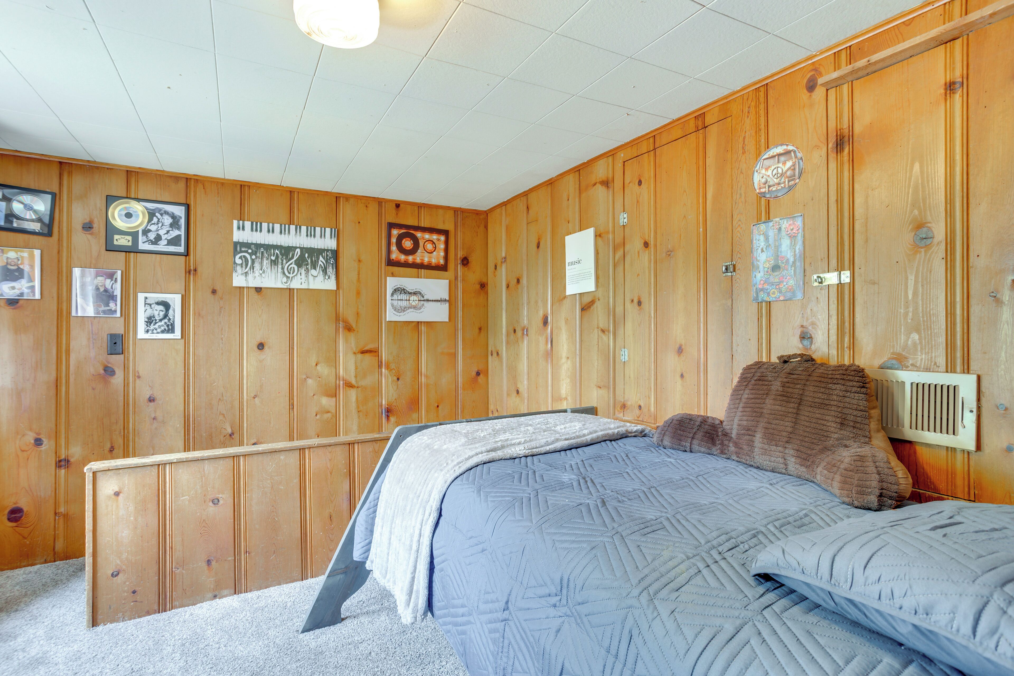Une chambre avec des lambris en bois, un lit recouvert d’une courtepointe bleue et divers tableaux encadrés accrochés aux murs.