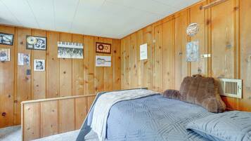 Une chambre avec des lambris en bois, un lit recouvert d’une courtepointe bleue et divers tableaux encadrés accrochés aux murs.