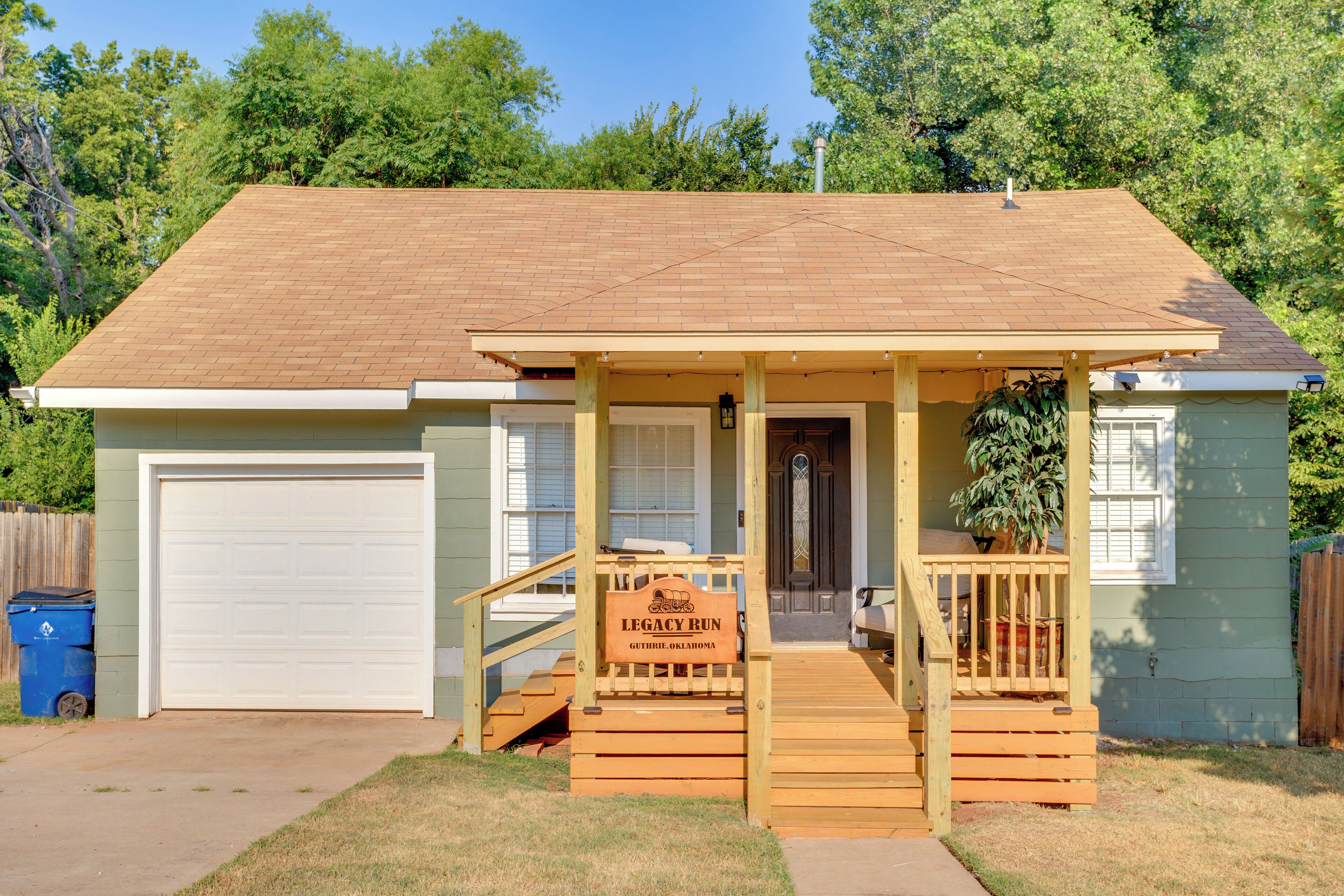 A single-story house with a garage, a covered porch with a wooden staircase, and a small front yard.