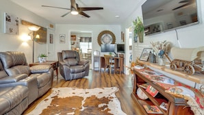 A living room with a leather sofa, a leather chair, a wooden coffee table, a cowhide rug, a ceiling fan, a flat-screen TV, a desk with a chair, and a bookshelf with decorative items. - Legacy Run: Guthries Historic Haven Near Shops (Guthrie)