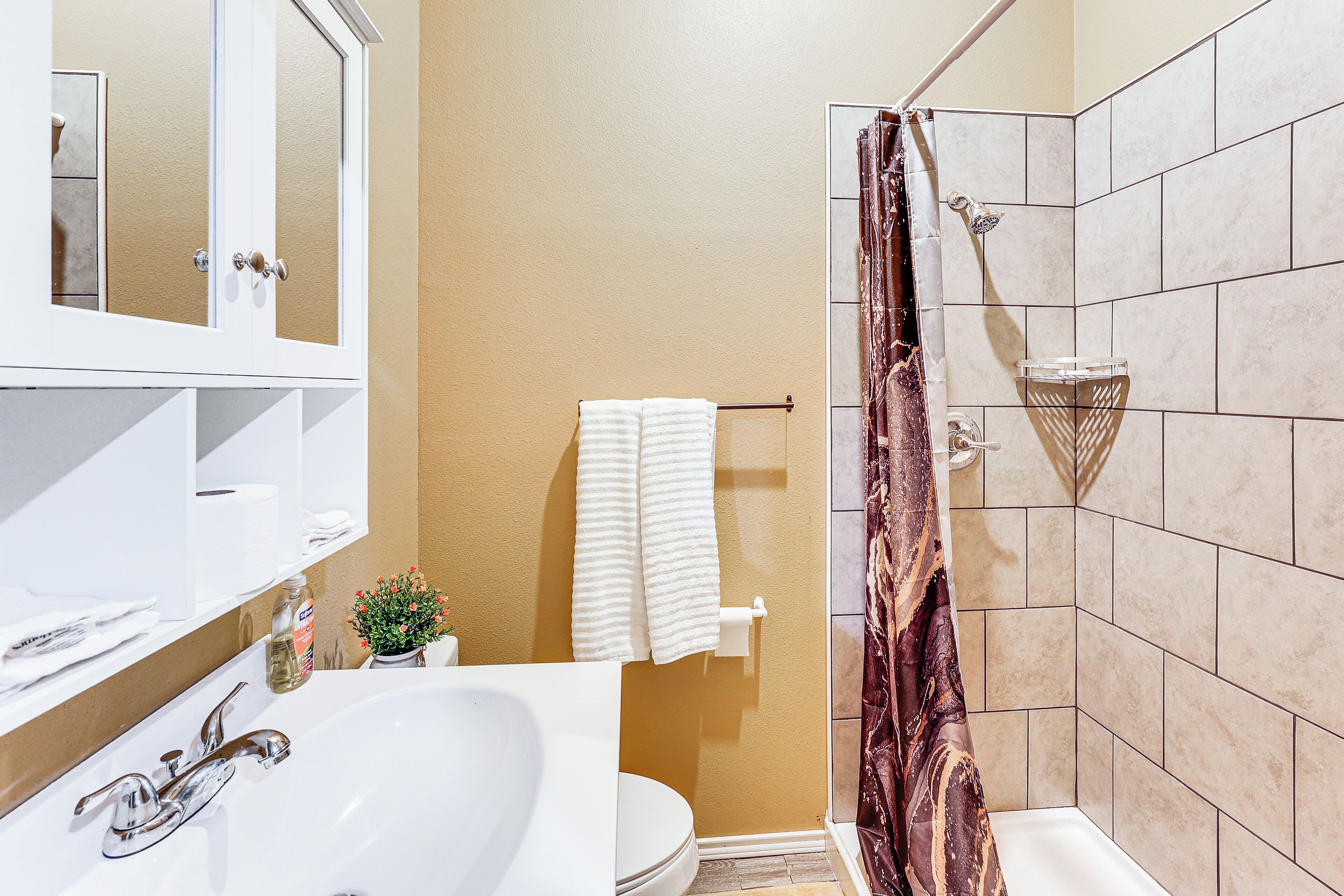 A bathroom with a white sink, a mirror, a toilet, and a shower with a curtain.