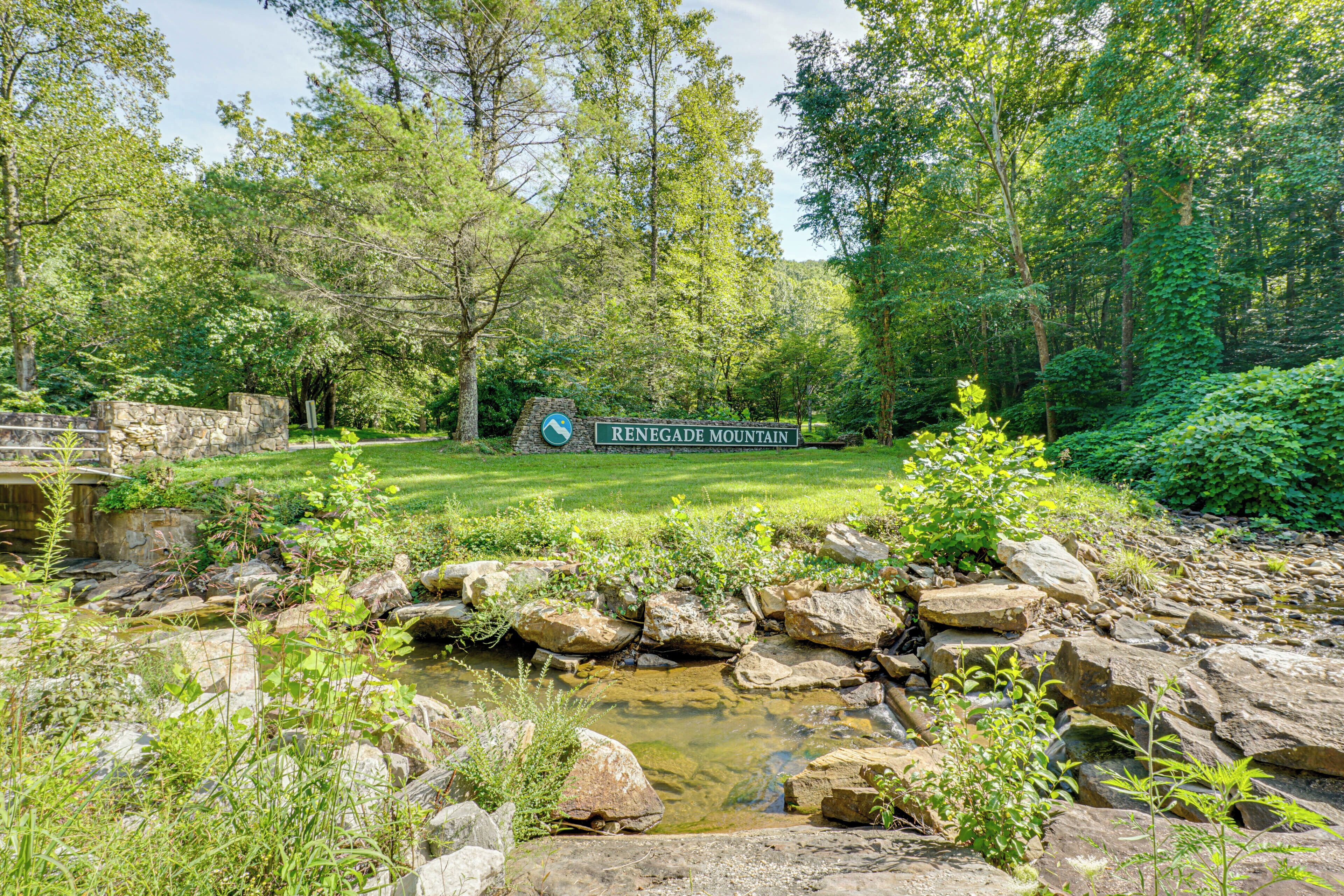 A sign for Renegade Mountain with a stone wall and a grassy area with a small stream.