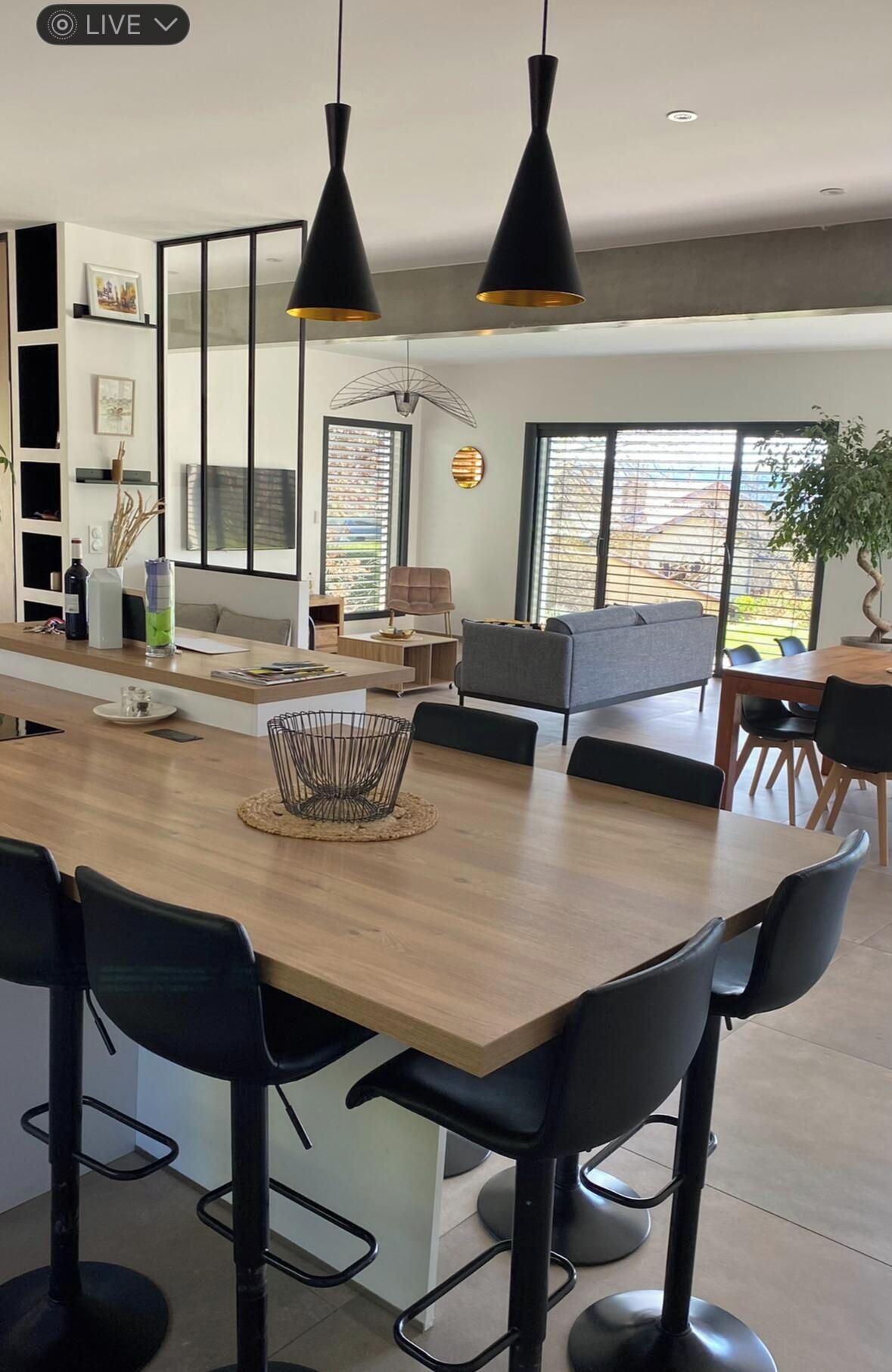 A modern kitchen with a central island, black bar stools, pendant lighting, and a view of the outdoors.