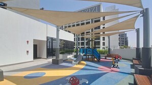 An outdoor play area with a slide, climbing structures, and a shaded seating area. - Azizi Riviera 61 - Serene Studio in Meydan (Meydan)