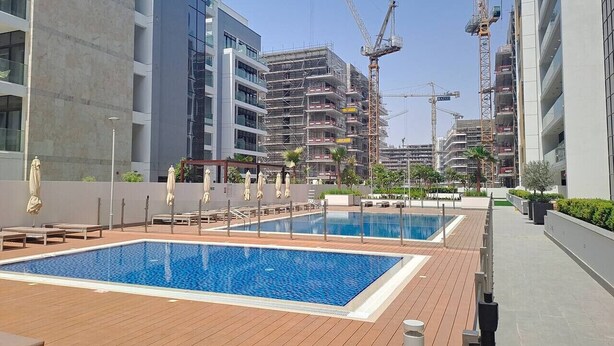 A rooftop pool area with multiple pools, lounge chairs, and umbrellas. - Azizi Riviera 61 - Serene Studio in Meydan (Meydan)