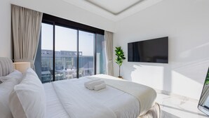 A modern hotel room with a large bed, a flat-screen TV, a potted plant, and a city view. - Azizi Riviera 61 - Serene Studio in Meydan (Meydan)