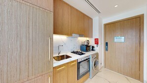 A modern kitchen with wooden cabinets, a sink, a stove, a microwave, and a washing machine. - Azizi Riviera 61 - Serene Studio in Meydan (Meydan)