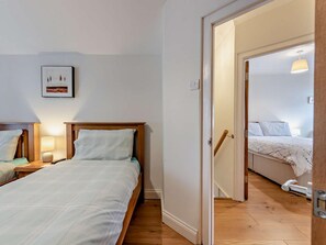 A bedroom with two beds, wooden headboards, and a nightstand with a lamp.