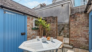 Een terras met een witte tafel en stoelen, een blauwe deur en een bakstenen muur.