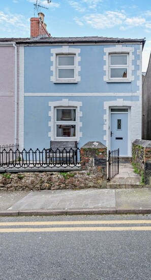 A two-story building with a light blue facade, a stone wall, and a black metal fence.