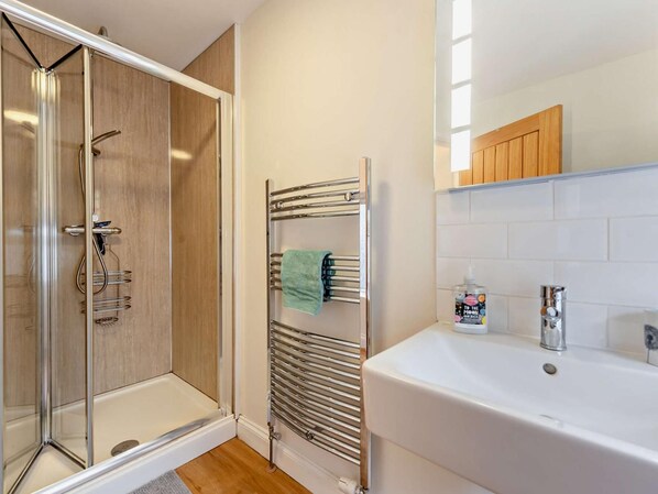A modern bathroom with a glass-enclosed shower, a built-in towel rack, and a white sink with a soap dispenser.