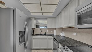 A modern kitchen with white cabinets, a stainless steel refrigerator, a microwave, and a built-in oven.