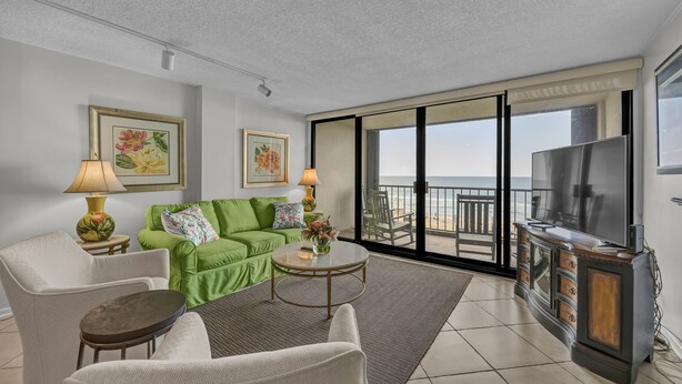 A modern living room with a green sofa, a white armchair, a round coffee table, and a TV on a wooden cabinet.
