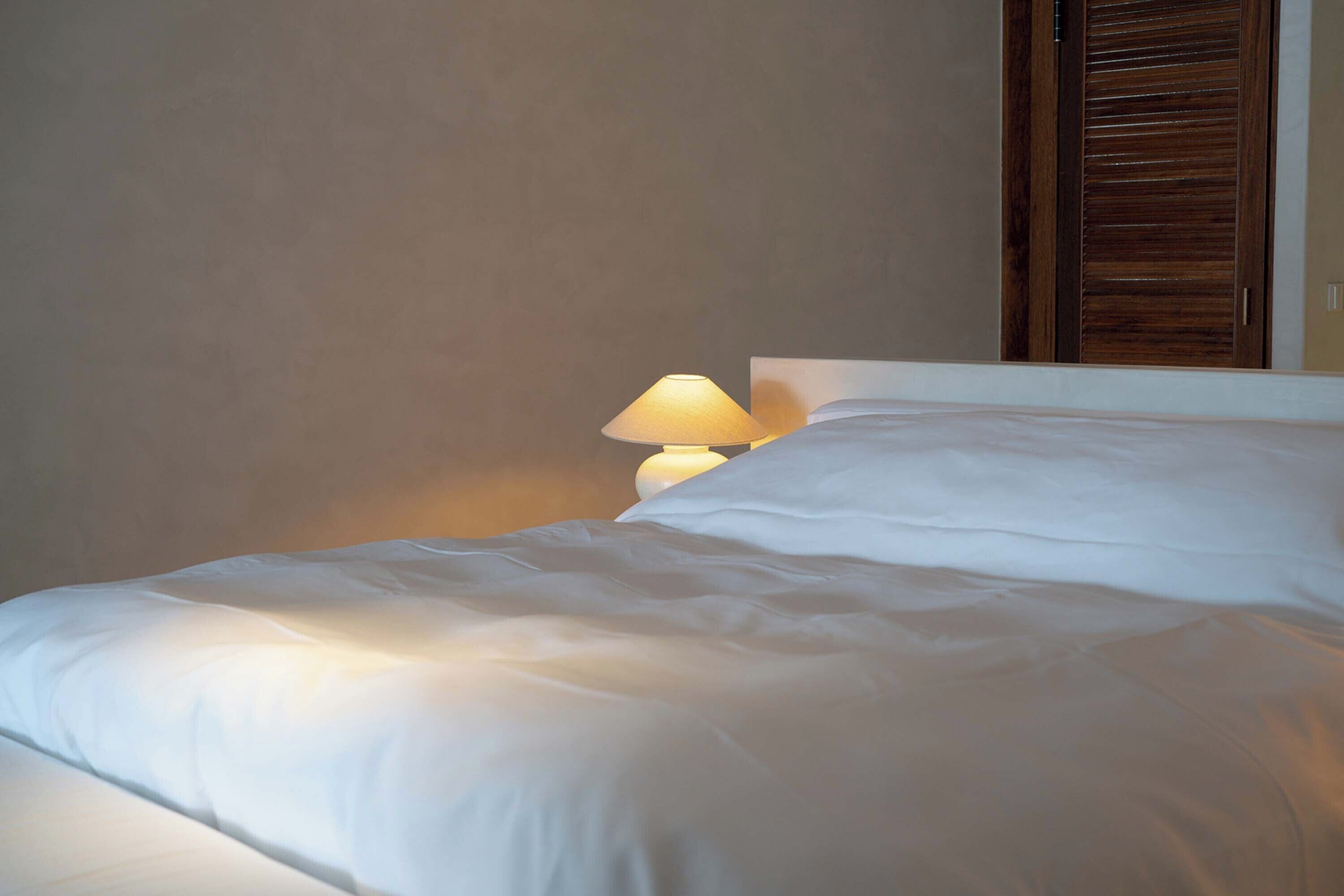 A neatly made bed with white linens and a bedside lamp.