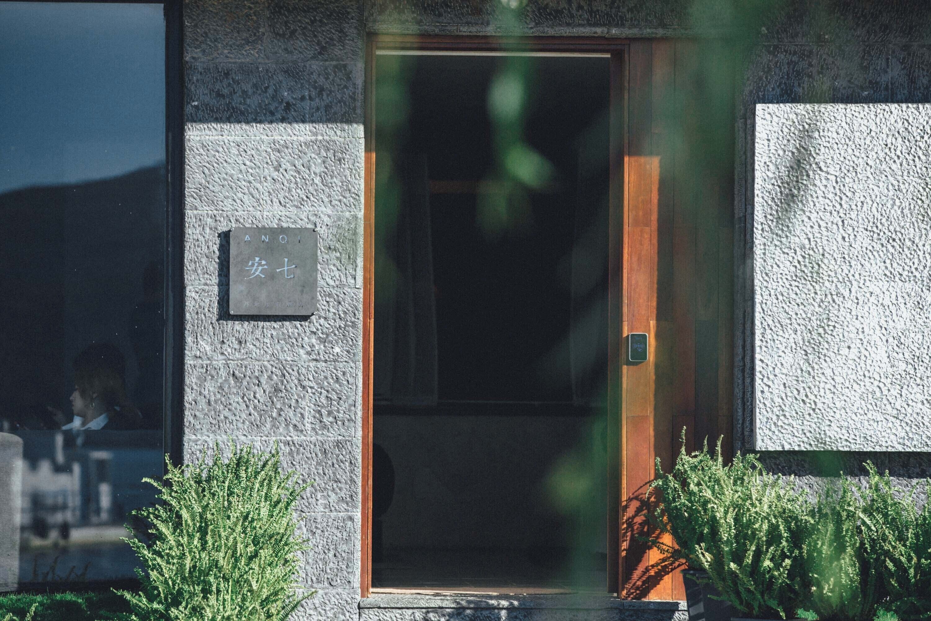 A building entrance with a stone facade, a wooden door, and a sign with characters.