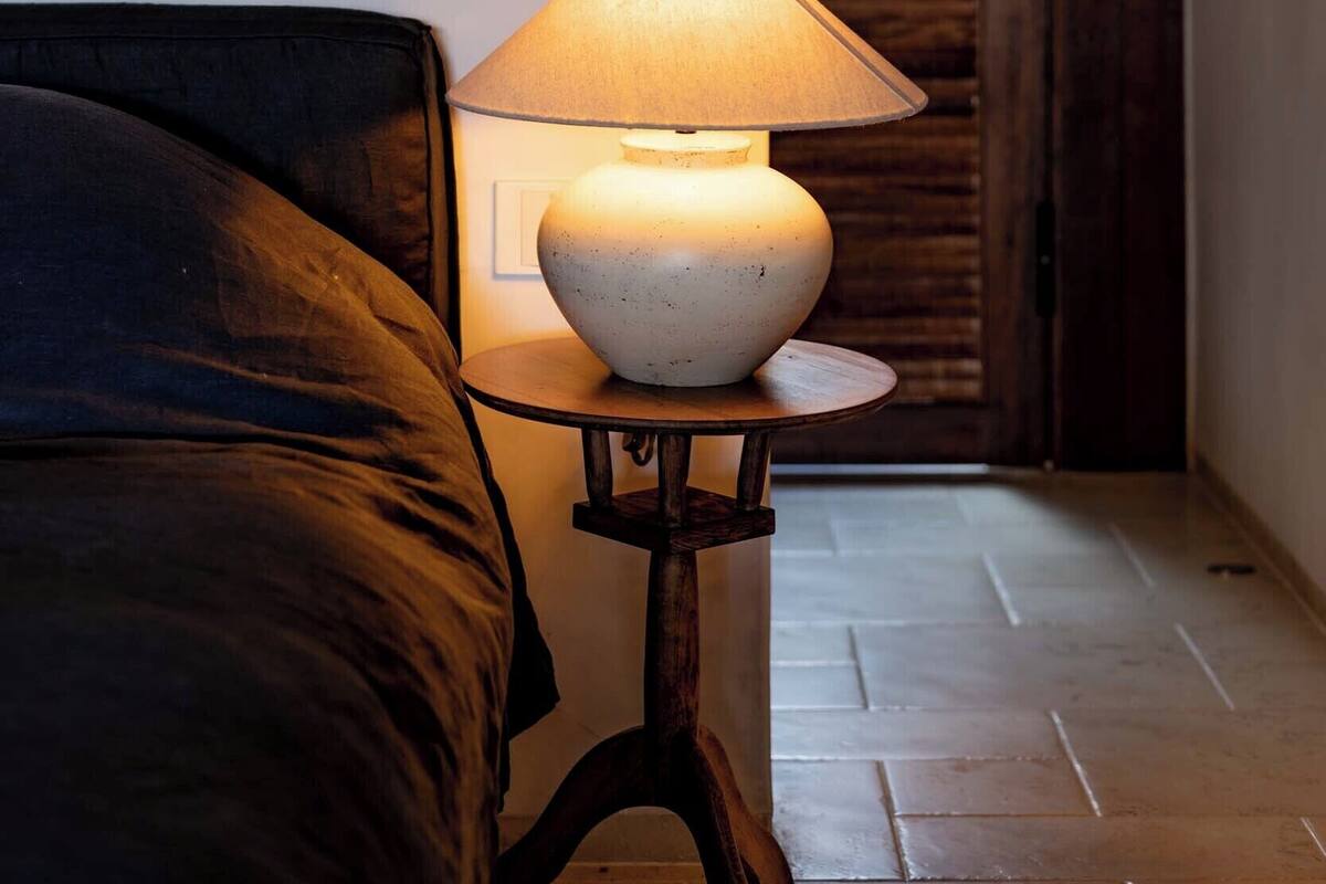 Un dormitorio con cama, una mesita de noche con lámpara, televisor montado en la pared y una puerta de madera con persianas.