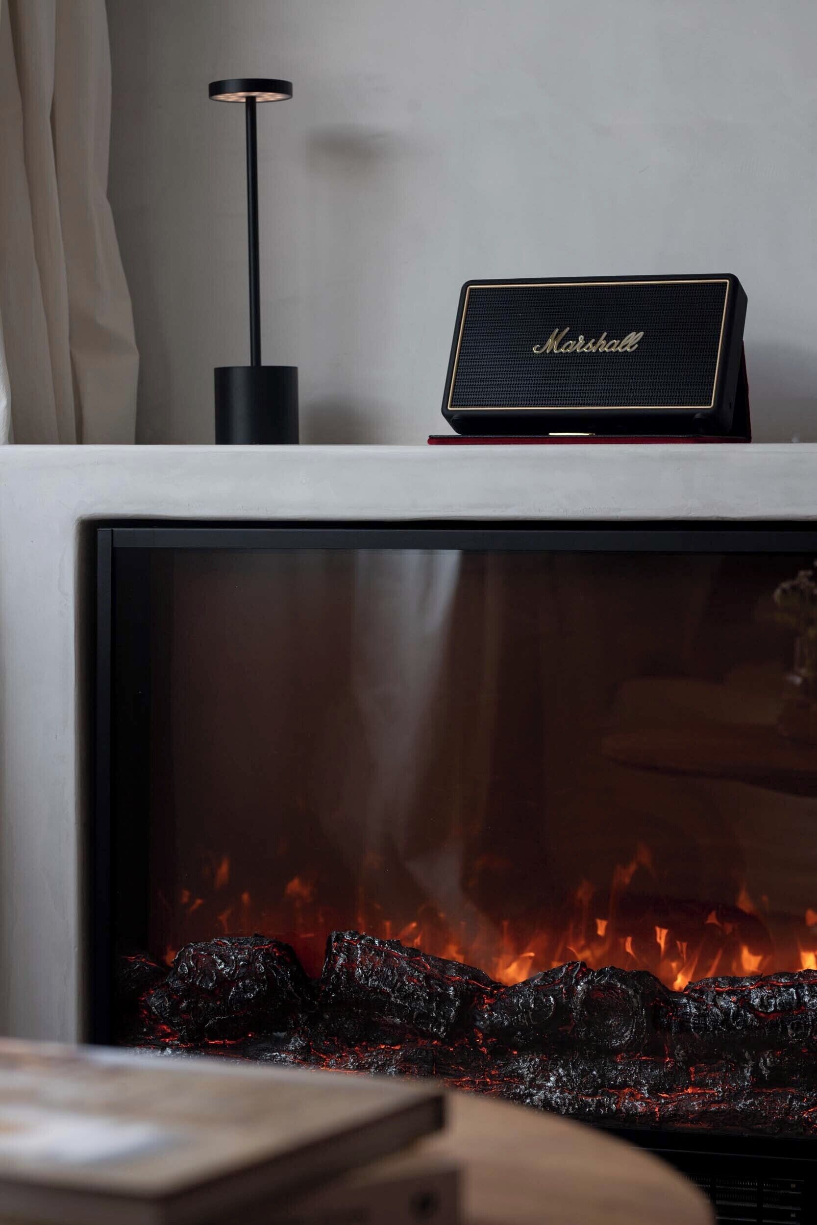 A fireplace with a Marshall speaker on top, a standing lamp beside it, and a visible fire.