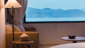Habitación de hotel con cama, sofá, mesita, lámpara y vistas al mar y a las montañas.