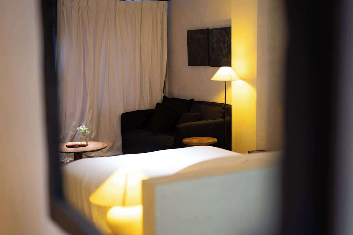 Una habitación de hotel con cama, un sofá, una mesita con un florero y una lámpara.